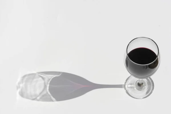 Glas rode wijn op een witte achtergrond met donkere diepe schaduw. — Stockfoto