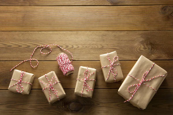 Vánoční pozadí. Dárkové krabice zabalené v řemeslném papíru na dřevěném pozadí. Pohled shora, rustikální styl. Kopírovat prostor. — Stock fotografie