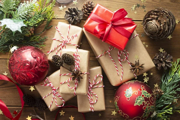 一组圣诞礼品盒用手工纸包着，枞树枝条，红色的灌木丛，木制桌子上的松果，为庆祝节日做好了准备。 顶部视图. — 图库照片