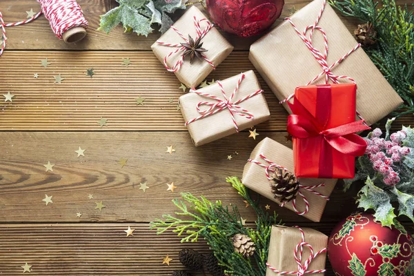 Vánoční ozdoby, dárkové krabice zabalené v řemeslném papíru, jedlové větve, červené ozdoby, borové šišky na dřevěném stole, sváteční svátky. Kopírovat prostor. — Stock fotografie