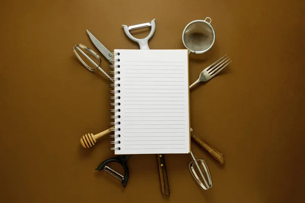 Cooking concept. Kitchen tools and empty note book. Brown background, top view.