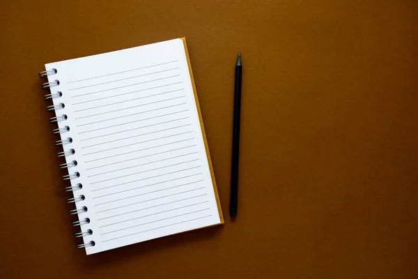 Open note book and pencil, brown background. Copy space.