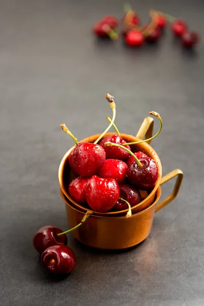 Fresh summer fruits, cherries in metal cups, grey background