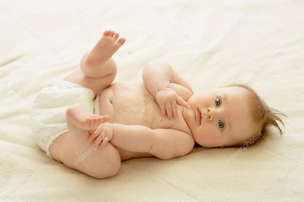 Newborn baby lying in bed. Baby touching his legs. Baby development, education, parenthood.
