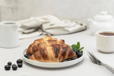 Taze kruvasanla kahvaltı, parlak arka planda çay ve yabanmersini. Hamur işi, çörek. Boşluğu kopyala.