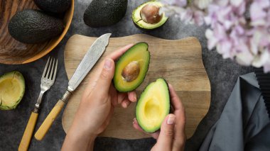 Avokado sosu pişiriyor, yayılıyor. Avokadoları kesme tahtasında tutan ve kesen kadın elleri. Sağlıklı yemek..