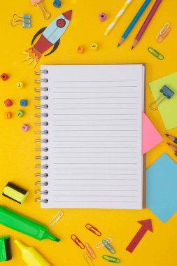Okul konseptine geri dönelim. Renkli roket, açık defter, okul malzemeleri. Sarı arka plan. Düz yat, boşluğu kopyala.