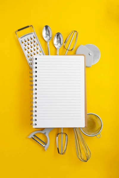 Keukengerei en open notitieboek voor recepten, gele achtergrond met ruimte voor tekst. Plat gelegd. Koken concept. — Stockfoto