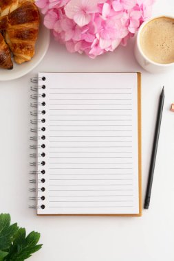 Masa üstü, çalışma odası, defter, bir fincan kahve ve kruvasan, pembe ortanca. Beyaz arkaplan.