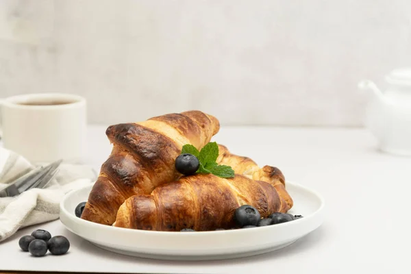 Café da manhã com croissants frescos, chá e mirtilo em fundo brilhante. Pastelaria, pães. — Fotografia de Stock