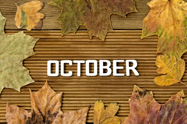 October word, letters with autumn dried leaves, over wooden background. Top view.