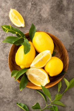 Koyu arka plandaki limonlar ahşap kasede. Yeşil yapraklı turunçgiller..