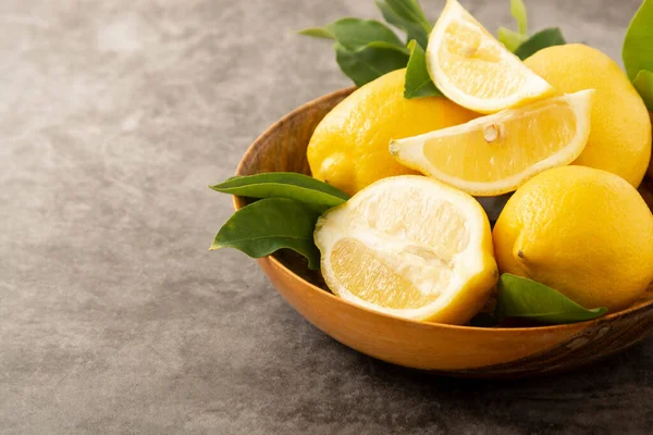 Koyu arka plandaki limonlar ahşap kasede. Yeşil yapraklı turunçgiller..