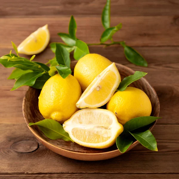 Koyu arka plandaki limonlar ahşap kasede. Yeşil yapraklı turunçgiller..
