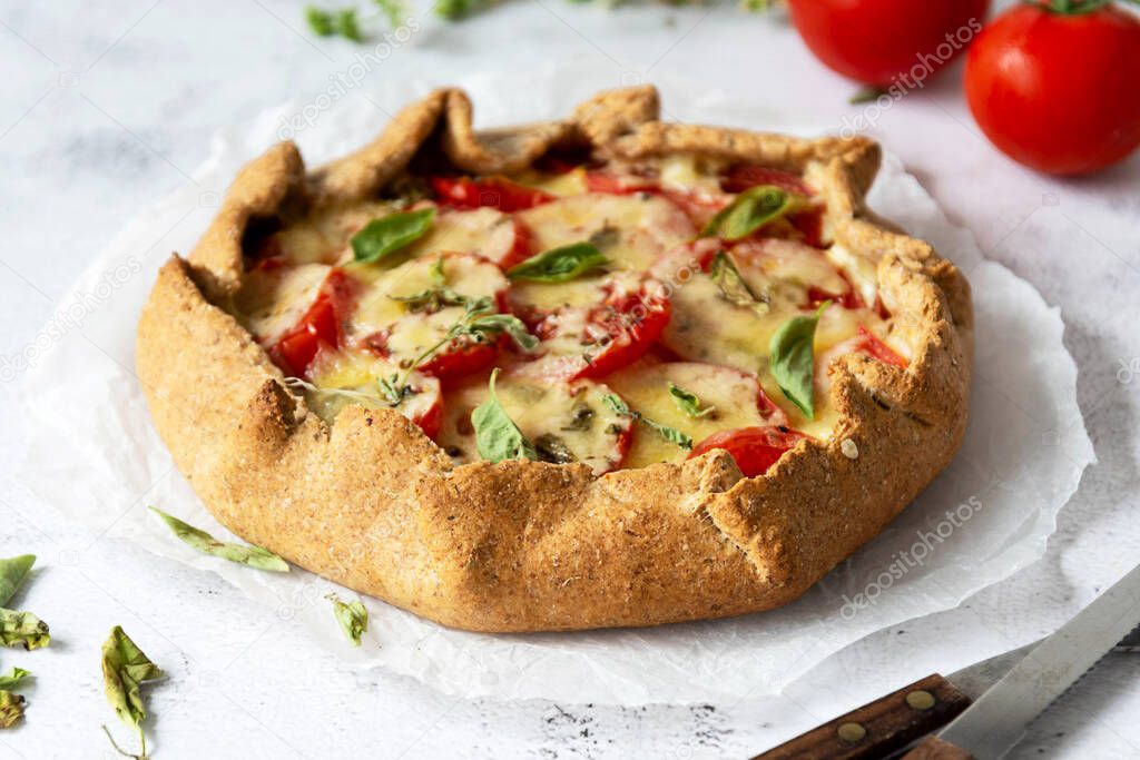 Homemade tomato tart or galette. Whole wheat rustic pie with tomatoes, cheeseand herbs. Healthy food concept.