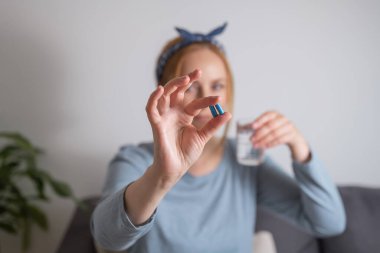 Mavi hapları parmaklarıyla tutan orta yaşlı bir kadın. Sağlık, beslenme takviyeleri, depresyon ve hastalıkların tedavisi