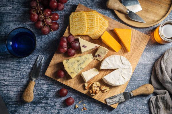 Сырная доска, различные виды сыра на доске, подается с виноградом и сухофруктами.