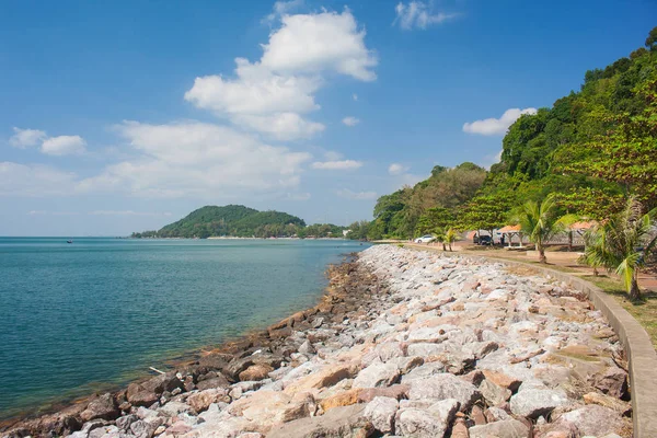 Yemyeşil ağaçlar ve arka planda mavi gökyüzü ile uzun sahil görünümünü tropikal deniz manzarası.