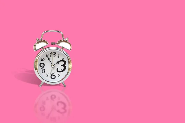Silver alarm clock isolated on pink background. (Selective focus)