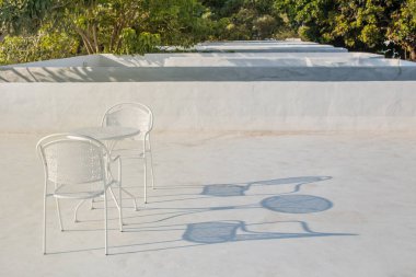 Beyaz metal masa ve sandalyeler kırsal kesimdeki ağaçlarla çevrili terasa yerleştirildi..