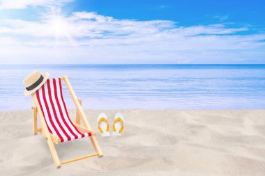 Yaz Tatili ve Tatil Gezisi Konsepti : Arka planda deniz ve mavi gökyüzünün güzel deniz manzarası na sahip kum plajında plaj sandalyesi, örme şapka ve beyaz sandalet parmak arası terlik.