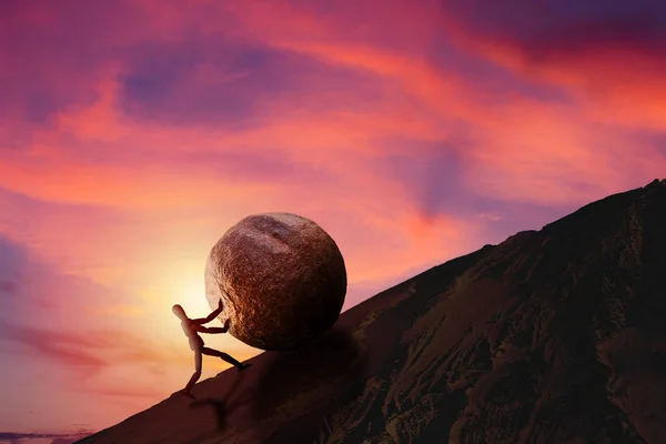 Business Challenge and Success Concept : Wooden figure pushing large stone uphill to top of mountain with sunset and beautiful sky in background.