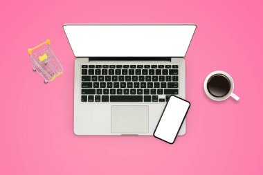 Online Alışveriş Konsepti: Laptop, akıllı telefon, sarı alışveriş arabası ve pembe arka plana konmuş kahve fincanı.