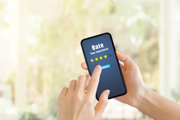 Customer Feedback Concept : Hand pressing feedback button on smartphone for giving best service ranking with blurred cafe restaurant or coffee shop in background.