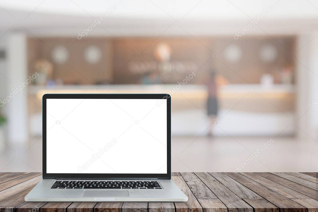 Business Travel and Communication Concept : Used laptop with blank white screen on wooden table and blurry image of luxury hotel lobby reception in the background.