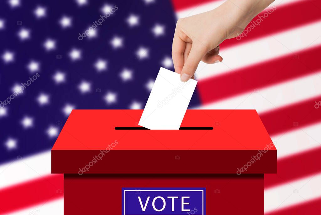US Elections Concept : Hand holding and putting voting paper in ballot voting box with USA flag in background.