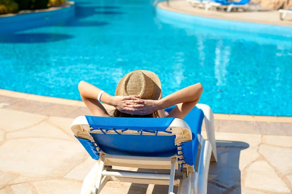 Mujer en un sombrero de paja relajante cerca de una lujosa piscina de verano, concepto de tiempo para viajar — Foto de Stock