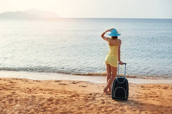 Bavul muhteşem deniz arka planda, seyahat için zaman kavramı ile bir şapka ayakta olan güzel kadın — Stok fotoğraf