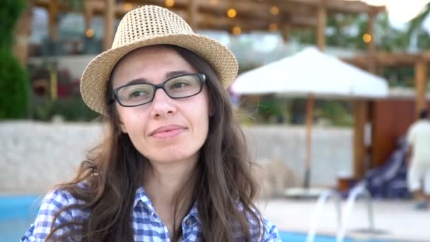 Profil einer jungen, hübschen Frau mit Sonnenbrille, die am Pool sitzt und sich an einem Sommertag im stylischen Badeanzug sonnt, im Hintergrund leuchtet das Poolwasser — Stockvideo