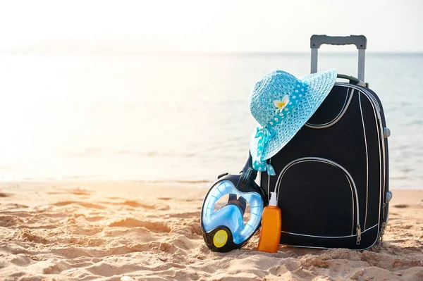 Suitcase and hat, sunscreen with a mask. The tropical sea, beach in the background. The concept of summer recreation travel and cruise traffic