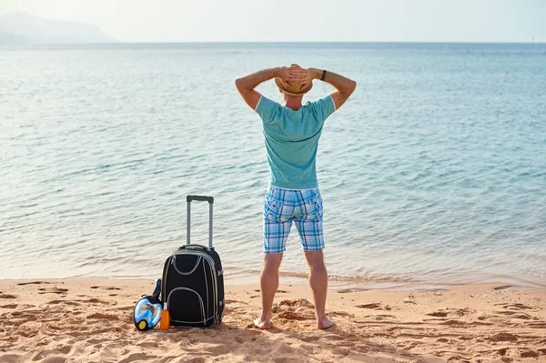 男子游客在夏天的衣服与手提箱在他的手, 看着海滩上的大海, 时间的概念旅行 — 图库照片