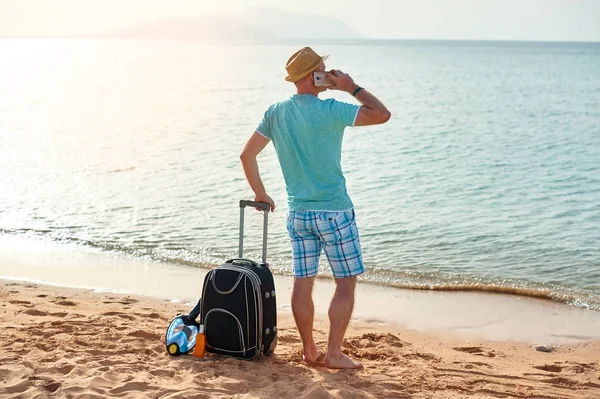 Mutlu adam bavul ve güneşli bir tatil plaj freelancer cep telefonu ayakta tam uzunlukta portresi — Stok fotoğraf