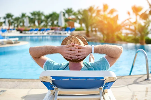 Отдых в бассейне летом. Молодой и успешный мужчина лежит на шезлонге в отеле на фоне заката, концептуальное время для путешествия — стоковое фото