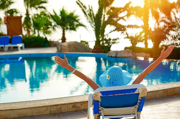 Femme dans un chapeau de paille relaxant sur une chaise longue près d'une piscine d'été luxueuse à l'hôtel, concept time to travel — Photo