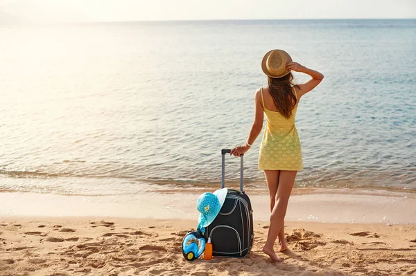 Gyönyörű fiatal nő, egy kalap állt a bőröndöt, a csodálatos tenger a háttérben, utazási idő fogalmának — Stock Fotó