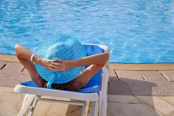Жінка в солом'яному капелюсі, що розслабляється на кріслі біля розкішного літнього басейну в готелі, концептуальний час для подорожей — стокове фото