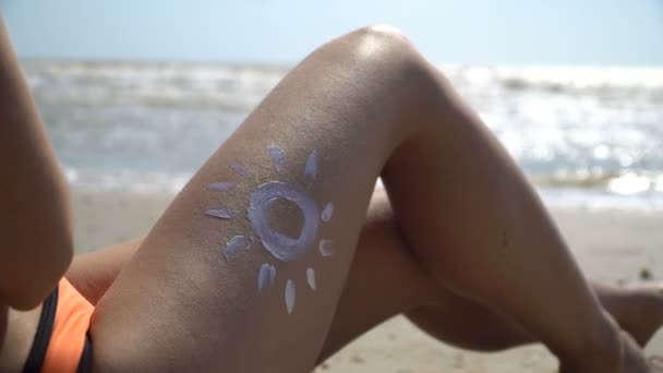 Mulher com sol pintado de creme na perna contra o mar — Vídeo de Stock