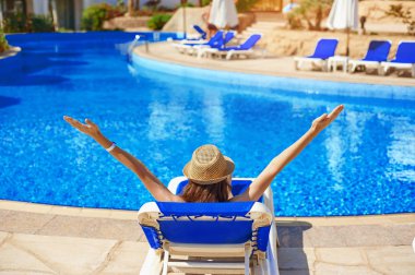 Kadın yakınındaki otel lüks yaz havuzda şezlong üzerinde rahatlatıcı bir hasır şapkalı kavram zaman seyahat etmek