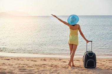 Bavul muhteşem deniz arka planda, seyahat için zaman kavramı ile bir şapka ayakta olan güzel kadın