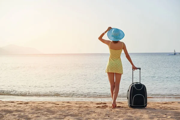 Beautiful young woman with a hat standing with suitcase on the wonderful sea background, concept of time to travel — Stock Photo, Image