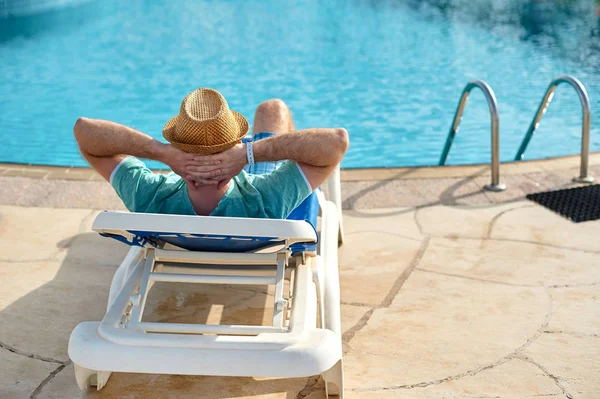 Relájese en la piscina de verano. Joven y exitoso hombre acostado en una tumbona en el hotel en el fondo de la puesta del sol, concepto de tiempo para viajar — Foto de Stock