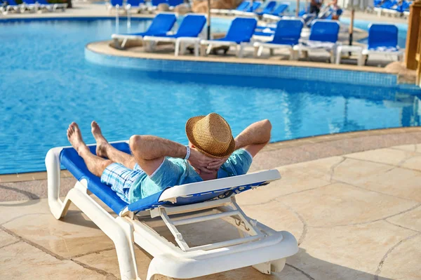 Relájese en la piscina de verano. Joven y exitoso hombre acostado en una tumbona en el hotel en el fondo de la puesta del sol, concepto de tiempo para viajar — Foto de Stock