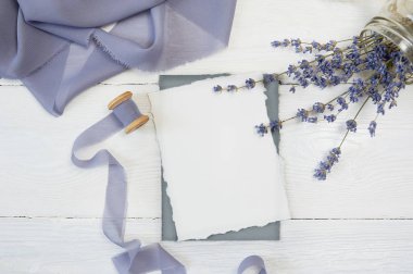 Mavi kurdele bir arka plan beyaz boş kart lavanta çiçekleri beyaz bir arka plan ile. Mockup zarf ve boş kartı ile. Düz yatıyordu. Üstten görünüm