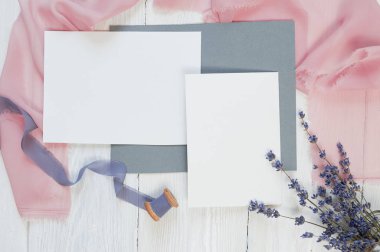 Kumaş pembe ve mavi bir arka plan üzerinde boş kartı kurdeleyle lavanta çiçekleri beyaz bir arka plan üzerinde beyaz. Mockup zarf ve boş kartı ile. Düz yatıyordu. Üstten görünüm