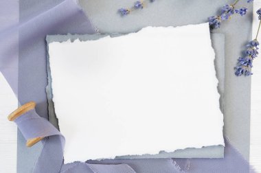 Arka plan mavi kumaş üzerinde boş tebrik kartı kurdeleyle lavanta çiçekleri beyaz bir arka plan üzerinde beyaz. Mockup zarf ve boş kartı ile. Düz yatıyordu. Üstten görünüm