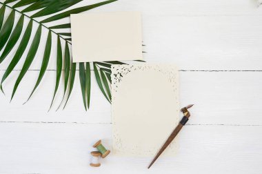 Palmiye yaprak bir zemin üzerine boş tebrik kartı şerit ve kaligrafi kalemi Beyaz ahşap zemin üzerinde beyaz. Mockup zarf ve boş kartı ile. Düz yatıyordu. Üstten görünüm